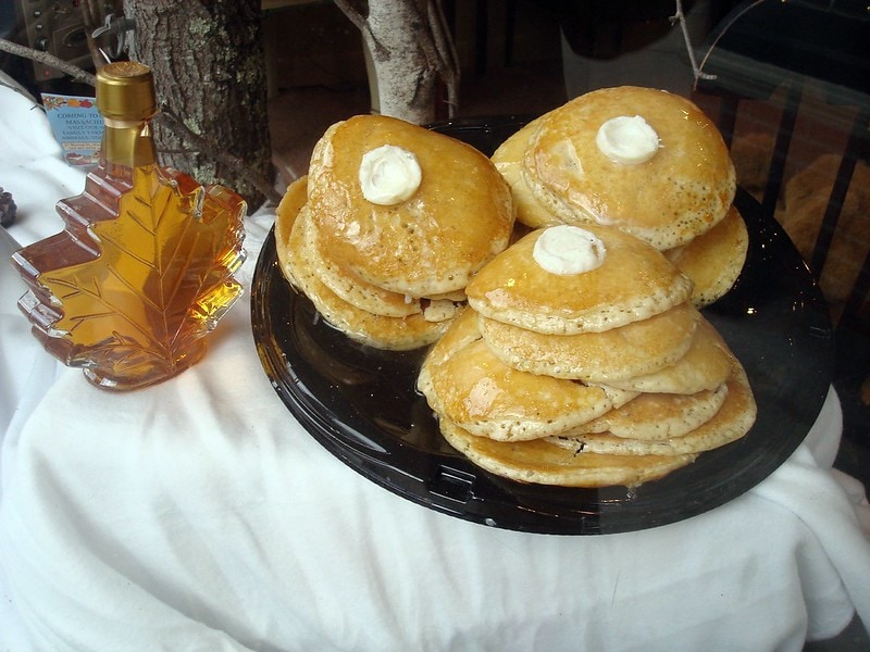 maple syrup in a canadian leaf bottle with stacks of pancakes with butter on top